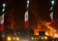 Foto: Bendera Iran berkibar saat api dan asap dari serangan Israel terhadap depot minyak Sharan membubung, menyusul serangan Israel terhadap Iran, di Teheran, Iran, 15 Juni 2025. (via REUTERS/Majid Asgaripour)
